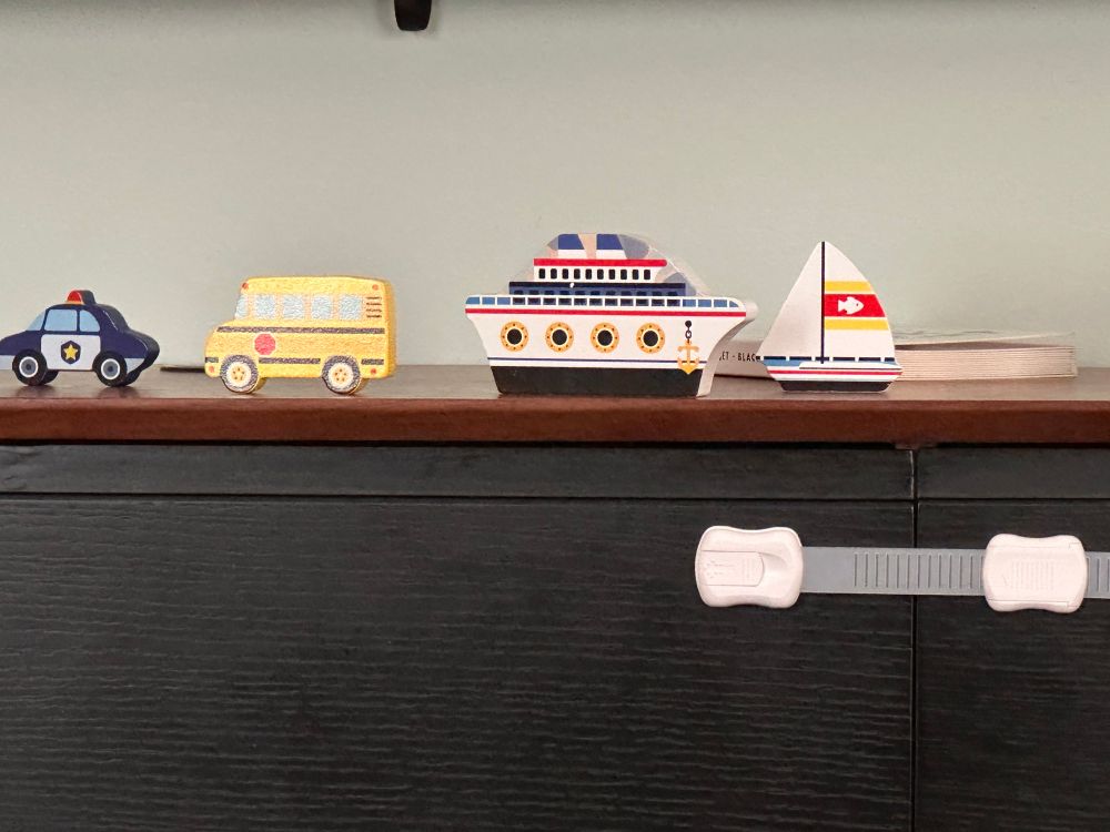 A collection of objects carved out of wood in the shape of a police car, a school bus, a ship, and a sailboat, respectively. They are sitting on top of a floating entertainment center.