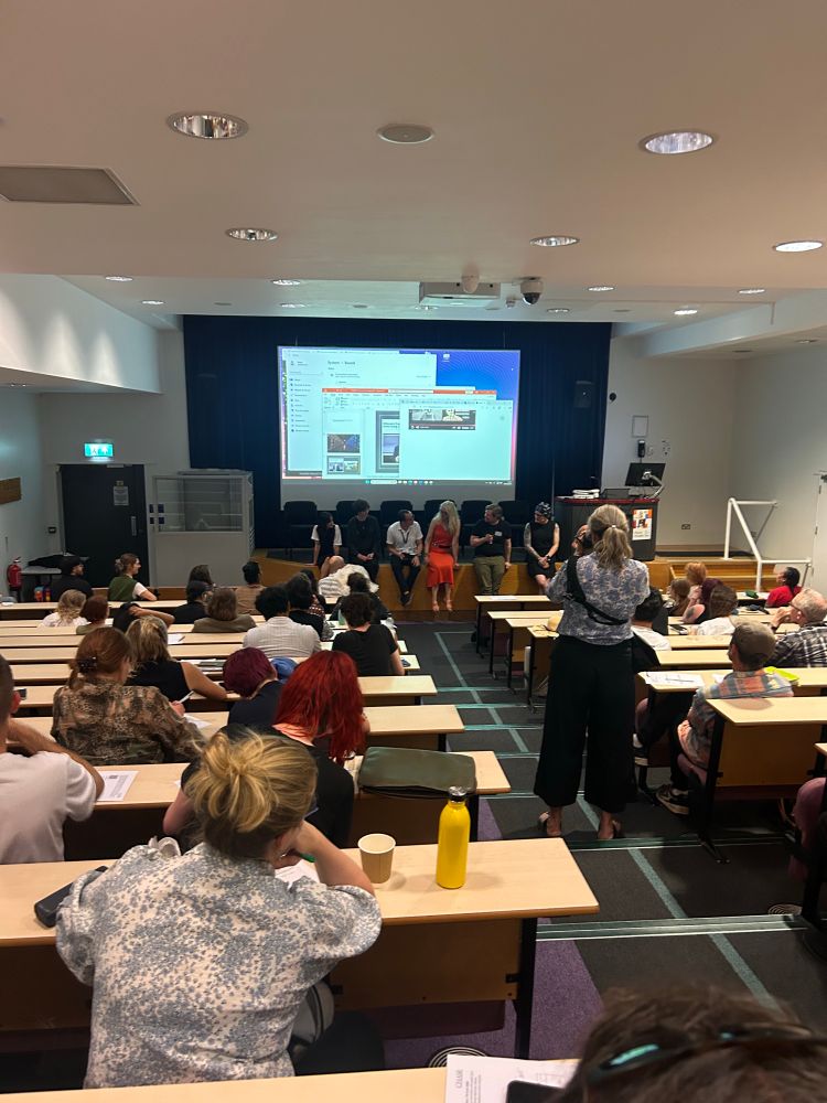 Seven of the organisers of CHASE Encounters sit on the edge of the stage in lecture theatre 
