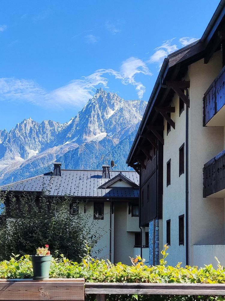 Mountains can be seen in the distance behind Alpine buildings. Clouds break up into waves as they get past the highest peak.