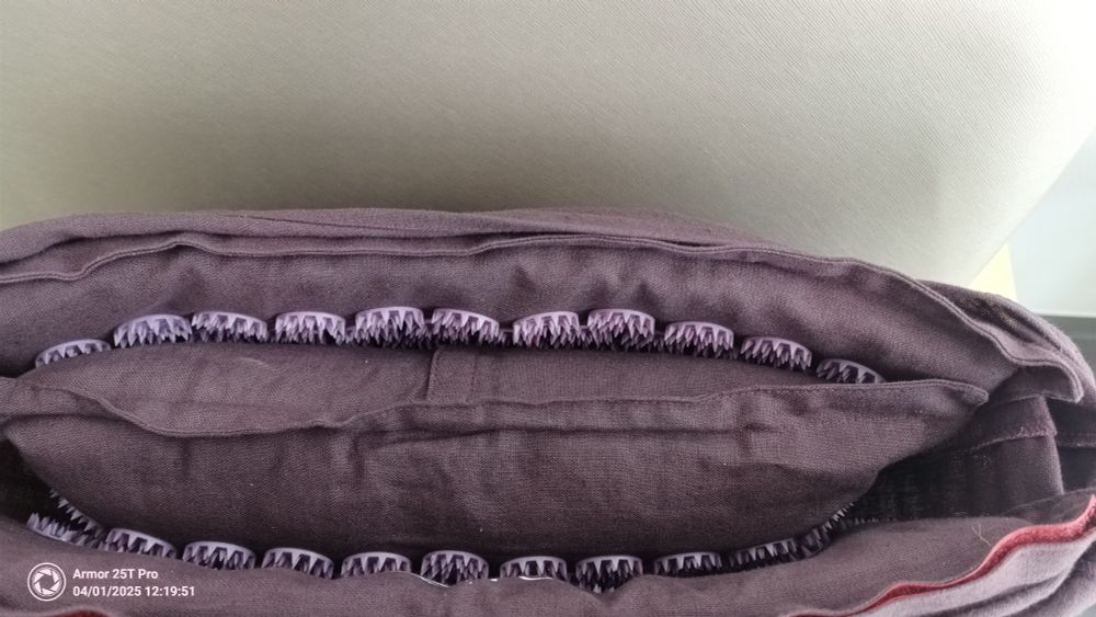 A foto of a brown -purplish bag.
Inside is a pillow of the same color.
Above and below the pillow are rows of round pinkish-purple plastic circles filled with sharp spikes.

(The pillow and the insides of the bag are actually an acupressure mat)