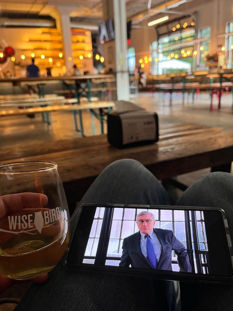 A man makes the correct life choice to always have Nancy Meyers THE INTERN downloaded on his phone while also having another phone to take a picture of said genius. Also an alcoholic beverage.