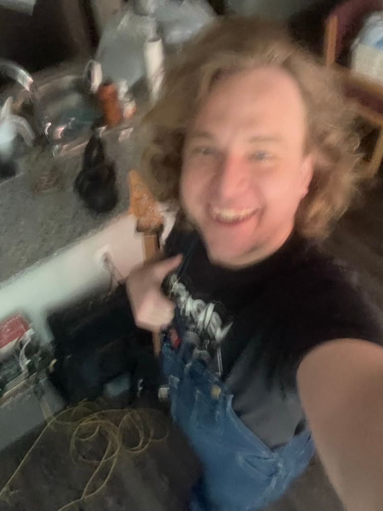 Man with hair and overalls contemplates playing bass