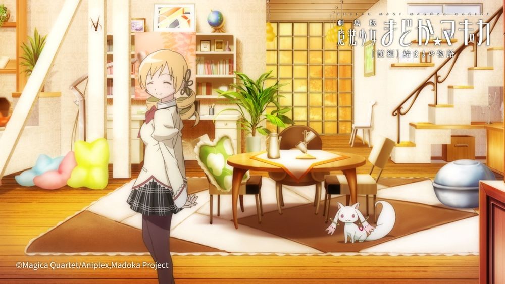 Tomoe Mami is smiling in her house, which is a comfy clutter of cushions and accessories. She has multiple cases displaying things and a table with mismatched plush chairs. A staircase leading upstairs is on the right. And Kyubey is just standing by the table I guess.