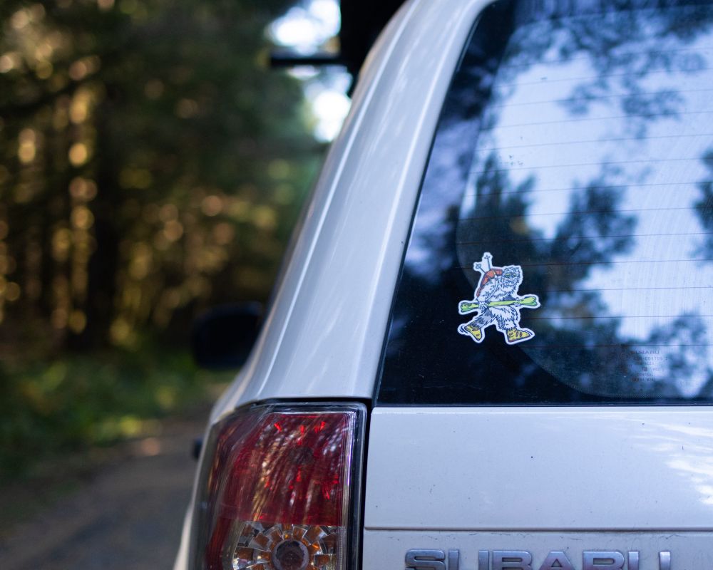 A photo of the back of a Subaru Forester. On the window is a sticker of a yeti in ski boots.