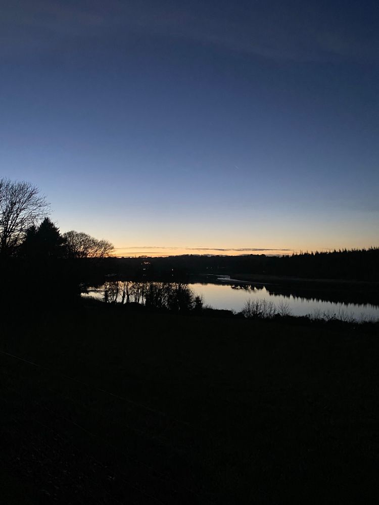 Evening sky, blue and gold over a river, landscape is black 