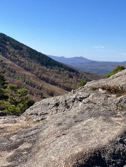 View of rock at the top onto part of a ski slop and mountains in the distance.