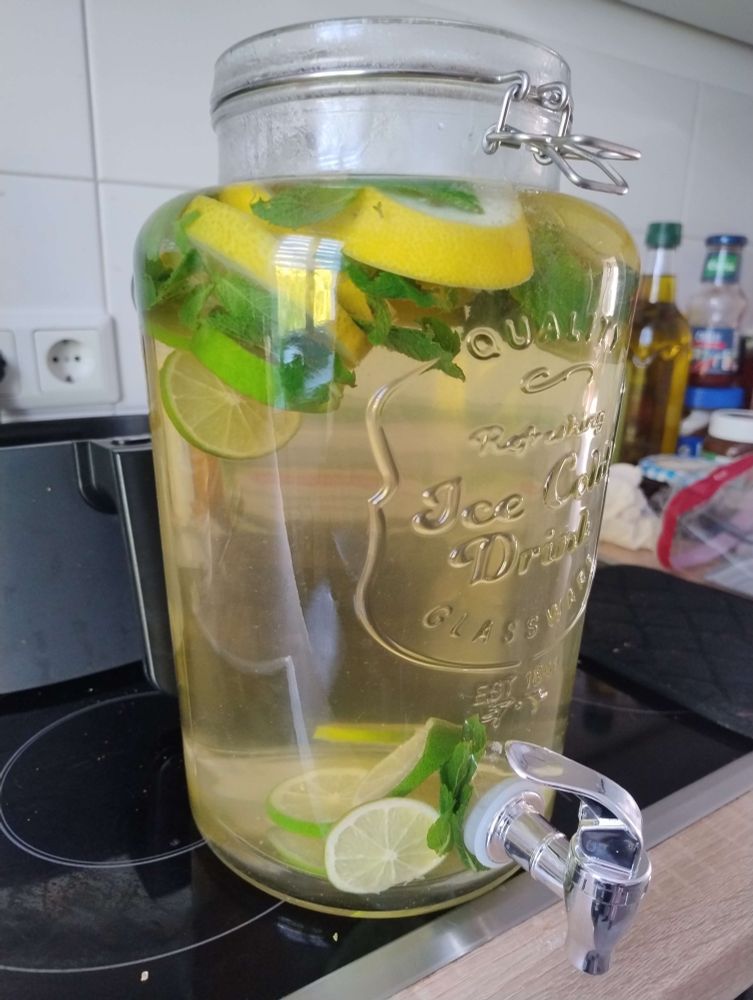 A large dispenser jar filled with water and slices of lemon, lime and mint leaves to infuse.