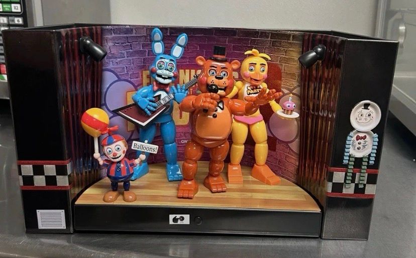 toy freddy, bonnie and chica, on a stage with balloon boy and a hollow back wall for popcorn