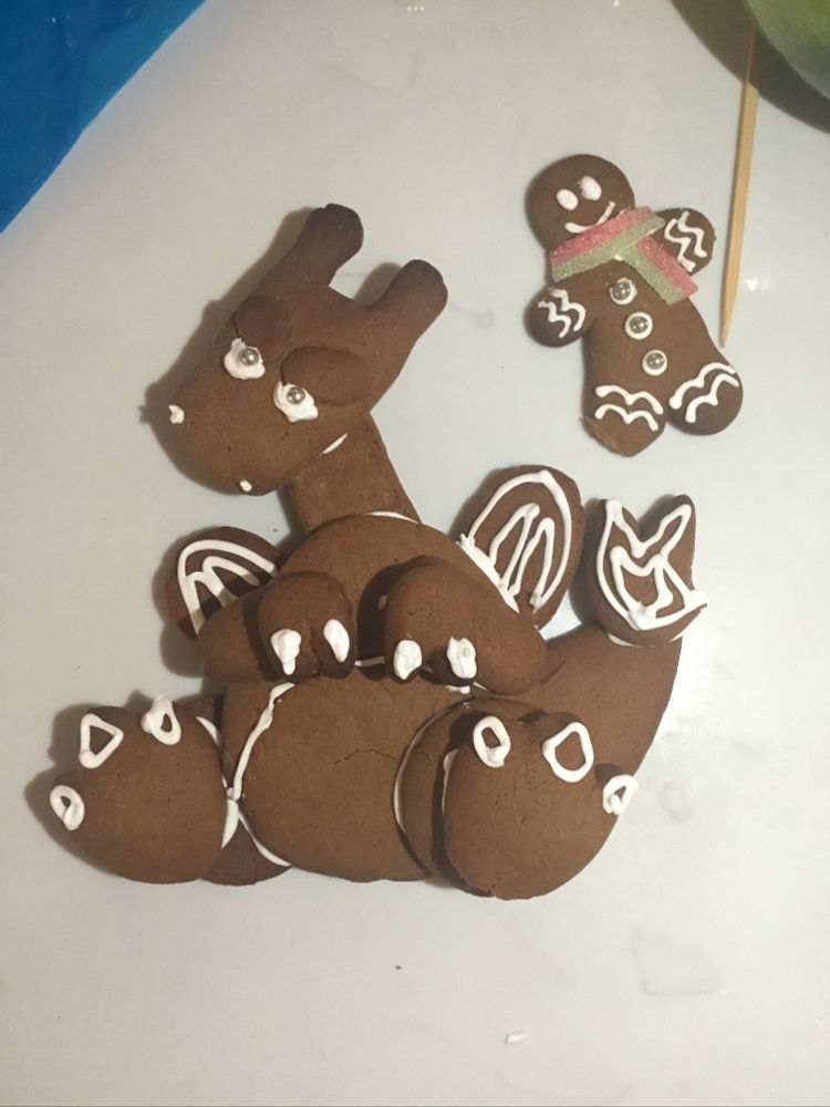 A Charizard from Pokemon made out of cookies, stuck together and decorated with icing. Next to them is a tiny gingerbread man to show how massive the charizard is in comparison.
