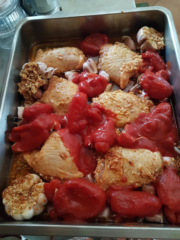 Haut de cuisse de poulet, beaucoup de têtes d'ail et tomates, le tout prêt à passer au four