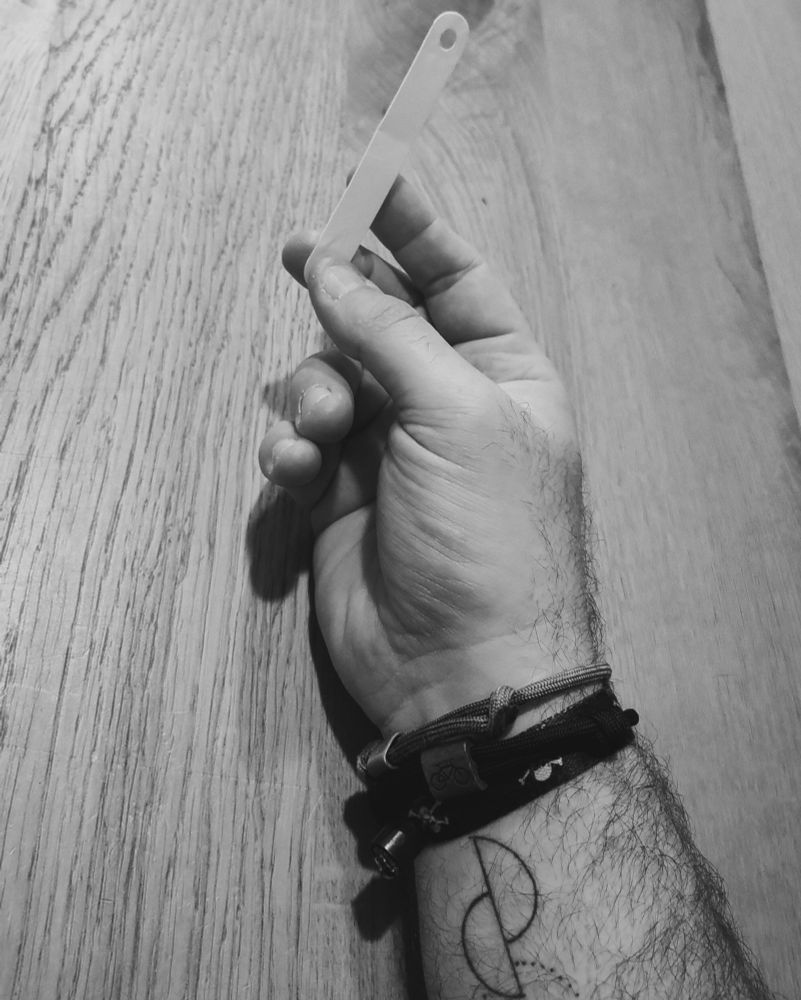 Eine Hand hält einen weisen Plastikstreifen mit 2 Löchern drin. Die Streifen werden in Schulmappen genutzt um die Blätter zu fixieren, bevor die Bügel umgeklappt werden. Der Fachbegriff ist dem Schreiber aber unbekannt.