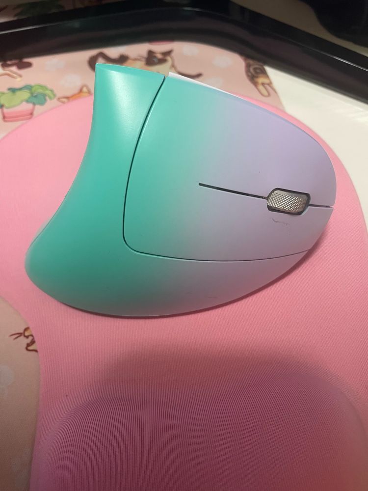 A mint green and light purple vertical computer mouse, with a point at the top, on a pink mousepad 