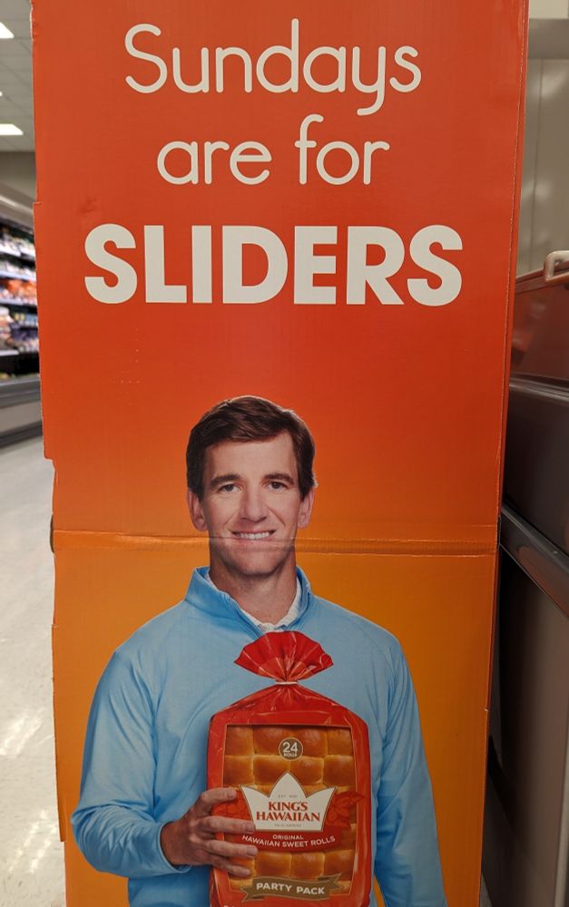 A grocery store display depicting a man with empty eyes and a pained expression while gripping a package of King's Hawaiian sweet rolls. Above his head reads "Sundays are for sliders"