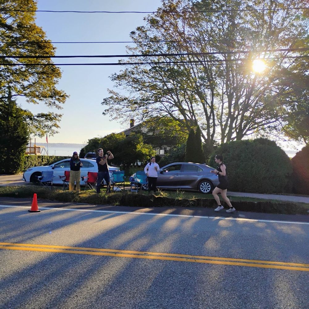 A woman running up a road with a slight incline with her mom, dad, and sister-in-law cheering her on and taking pictures.