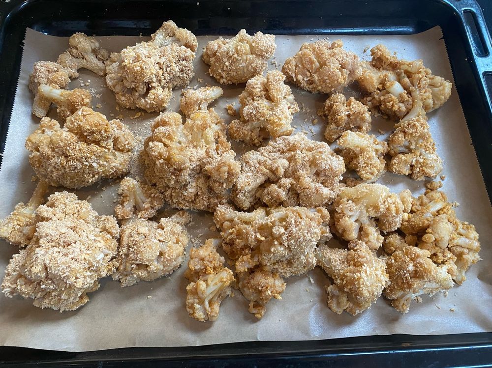 Ein Backbleck mit Backpapier, darauf Blumenkohlrößchen die bräunlich schimmern und in Pankomehl gewendet sind. 