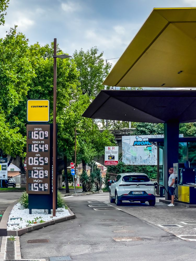 Ein Tankstelle mit einem Auto. Der Fahrer betrachtet das Schild mit den Preisanzeigen aller Kraftstoffe.