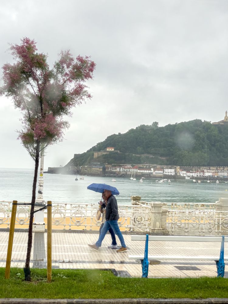 Zwei Spaziergänger mit Regenschirm an der Strandpromenade.