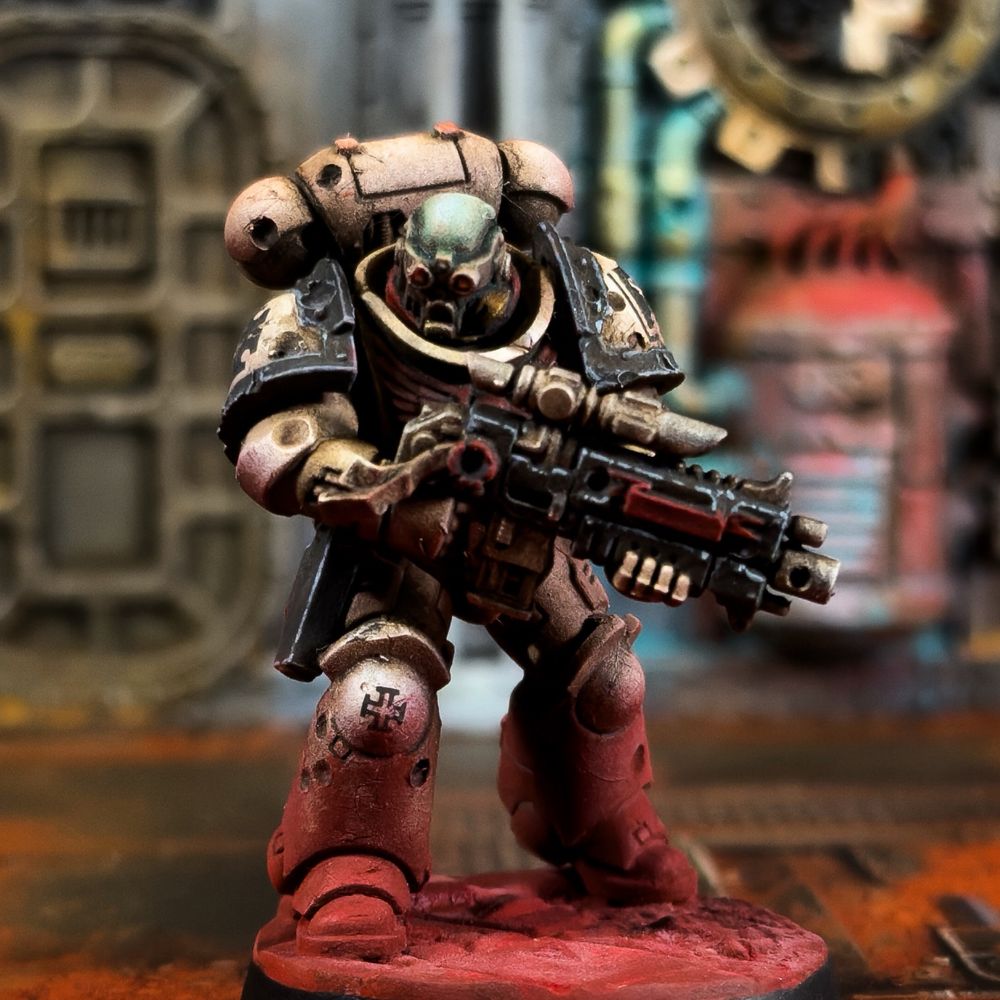 A Tome Keepers intercessor painted in the Grimdark style. His head is bare, but he is wearing red goggles - perhaps to help with marksmanship. He is armed with a stalker pattern bolt rifle. His armour is bone with black trim and weapons, with red details like the Aquila. He is looking battle-beaten and grimy, like he’s been in the field for a very long time. His base and lower legs are caked in red dust.