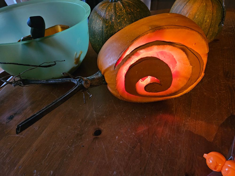 Photo of a lit jack-o-lantern. The pumpkin is carved into a spiral, ending in a stem that splits into two branches