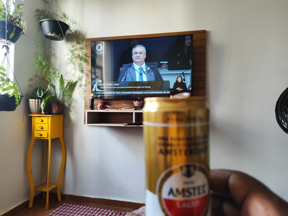 Foto de uma lata de cerveja para comemorar o julgamento do Jair.....ao fundo a tv com a imagem do ministro Dino 