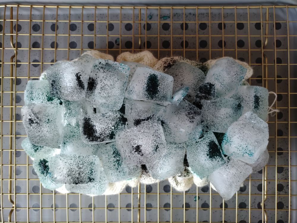 Top down photo of knitted fabric crumpled on a wire rack, it is covered in ice with powdered dye sprinkled around.