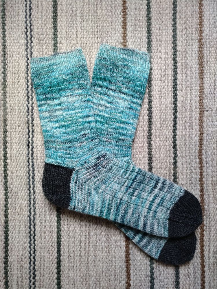 Photo of knit socks in teal and dark grey colours on a striped rug
