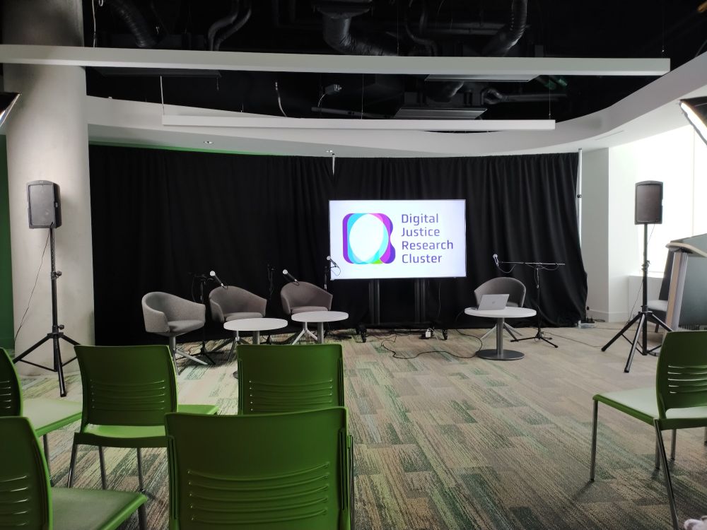 Conference room with green and grey chairs in front of a screen that says Digital Justice Research Cluster