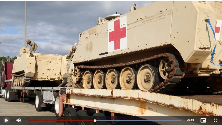 M113 armoured personnel carriers being loaded onto a low loader. They are dust yellow and one has a red and white medical cross on side