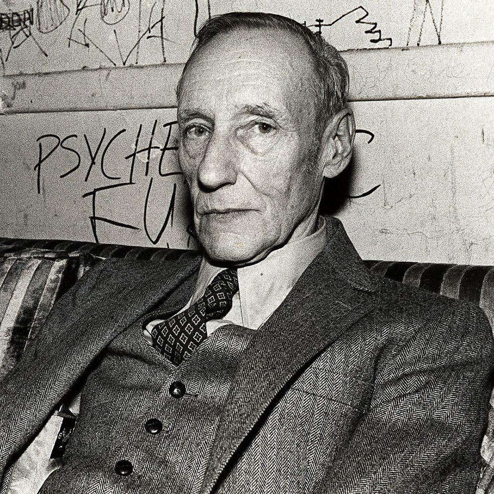 William Burroughs, sitting in front of a graffiti covered wall.
