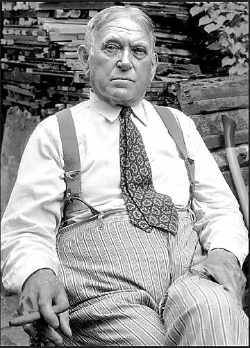 H. L. Mencken, sitting in a chair and smoking a cigar.