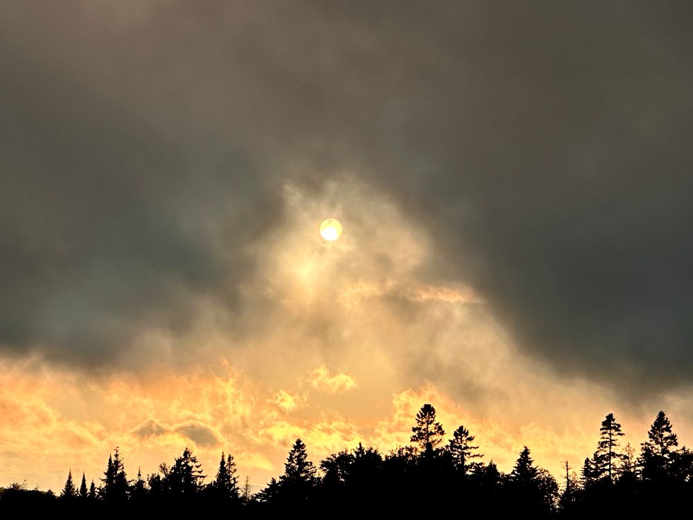 Drapes of dense green-black clouds rise and descend over a late-afternoon sun dulled flat white by distant forest fire haze