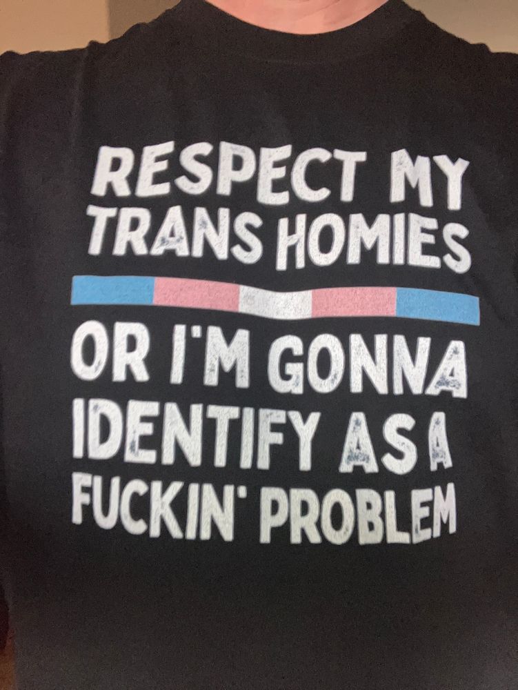 Picture of a black T-shirt with a “Respect my trans homies or I’m going to identify as a fuckin’ problem” in white text, separated by a band in the colours of the Trans flag.
