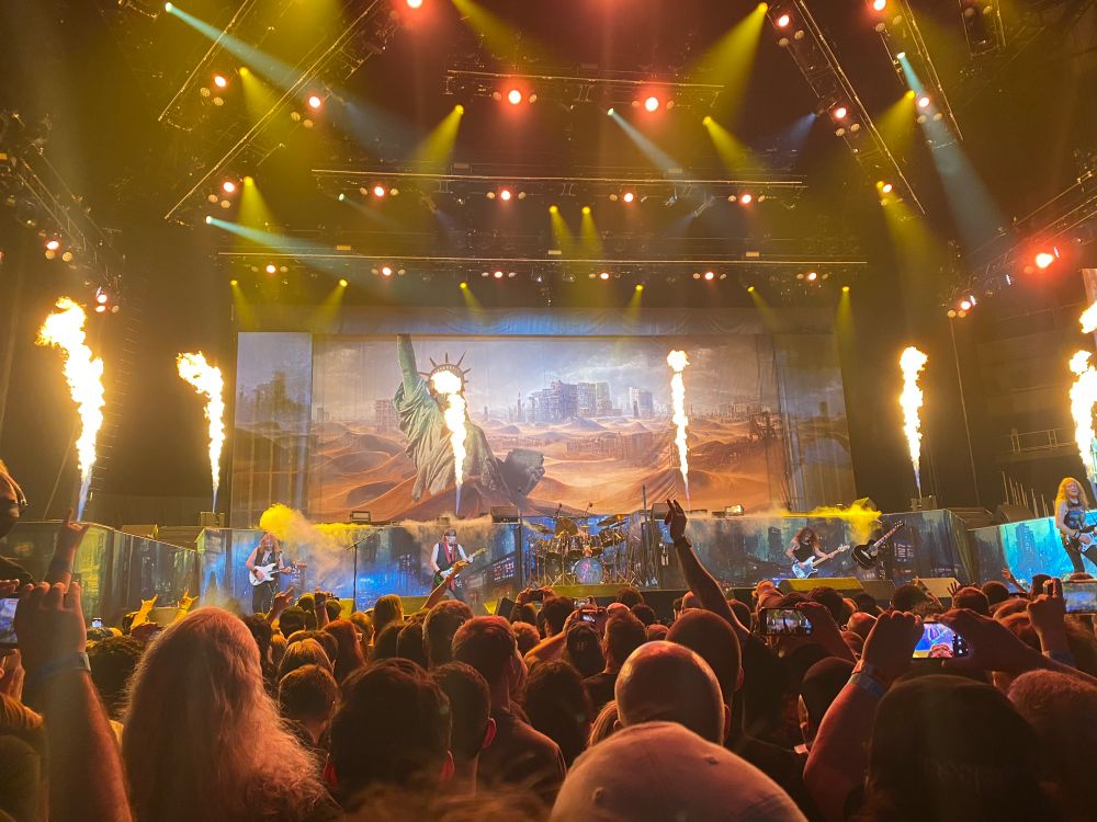 The metal band Iron Maiden playing on stage with yellow stage lights and vertical columns of flame