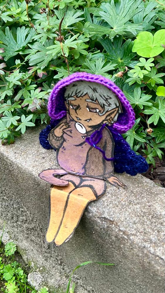 Photo de la Consœur du jour : il s'agit d'une petite vampirette aux cheveux courts et argentés qui câline son petit chat démon cyclope violet (qui est un petit animal récurrent de mes inktober !). Elle est assise sur le rebord d'un petit parapet avec derrière des plantes.