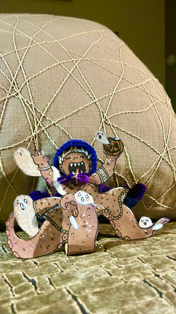 Photo de la dernière Consœur de ce mois-ci : il s'agit d'une joviale créature affublée de 3 gros tentacules en guise de jambes, elle porte une robe à pois et a des denrs pointues. Elle lève les bras en l'air et est entourée de petits fantômes, notamment un qui sort d'une citrouille de Halloween dans sa main gauche. Elle s'ambiance dans ma chambre d'hôtel à Glasgow ✌️