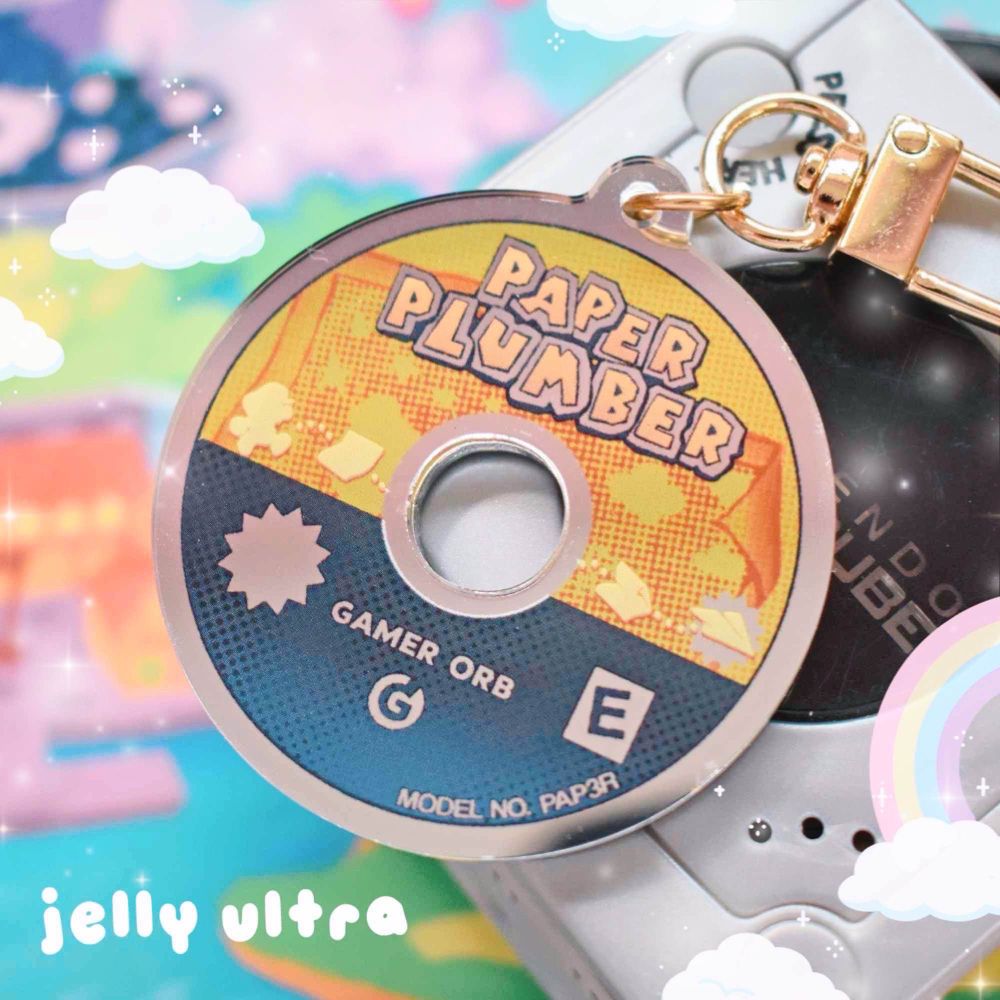 mirror acrylic charm made to look like a miniature game disc. Parodies a game about a Paper Plumber. Text reads "GAMER ORB", rated E for everyone. Model number text includes leet speak for
"PAPER"