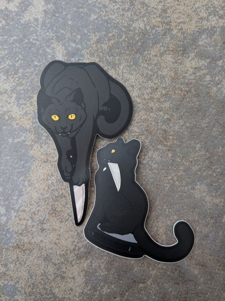 stickers of black cats with knives. One is holding a knife with its paws and the other is sitting on a roomba with a knife in its mouth. 
