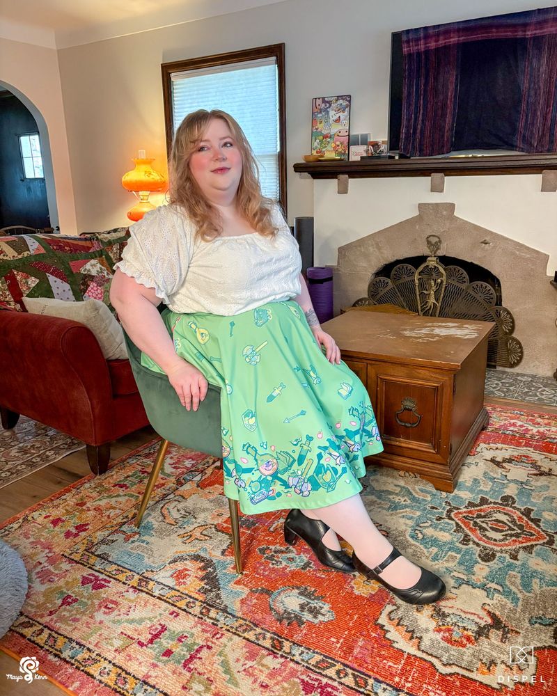 maya sitting in the new dispel dice collab skirt. she's wearing a 2-3xl. the design is clearly visible over the knees