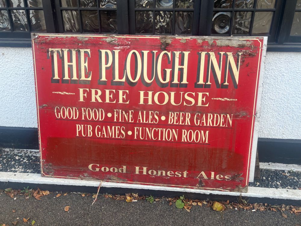 Old pub sign reading ‘THE PLOUGH INN - FREEHOUSE - Good Food * Fine Ales * Beer Garden * Pub Games * Function Room * Good Honest Ales