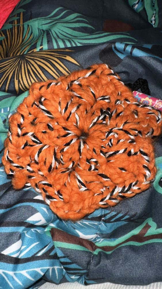 A crocheted hexagon in pumpkin orange colored Lion Brand Wool-Ease Thick and Quick held double with a black and white marled LIon Brand Anti-Plying yarn