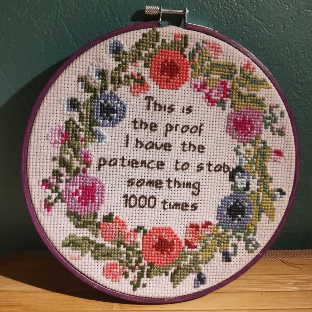 Point de croix avec écrit "this is the proof i have the patience to stab something 1000 times", entouré d'une couronne de fleurs roses, violettes et bleues