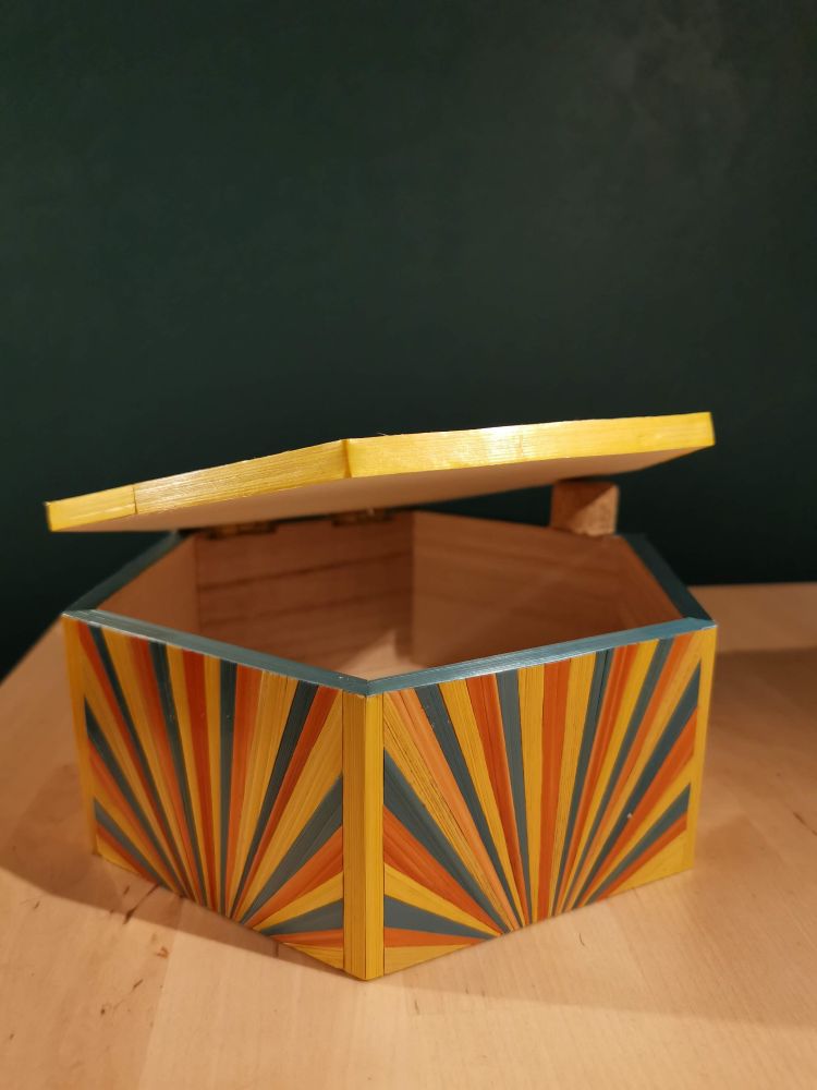 Boite hexagonale en marqueterie de paille, avec un caneton jaune façon origami, sur fond turquoise, sur le couvercle. Les côtés sont en motif soleil jaune, turquoise et orange 