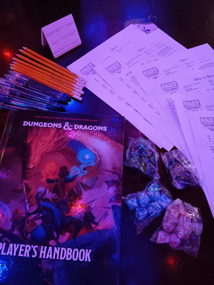 Pre-generated character sheets, pencils, pens,  dice sets, and a Dungeons & Dragons Player's Handbook on a wood table