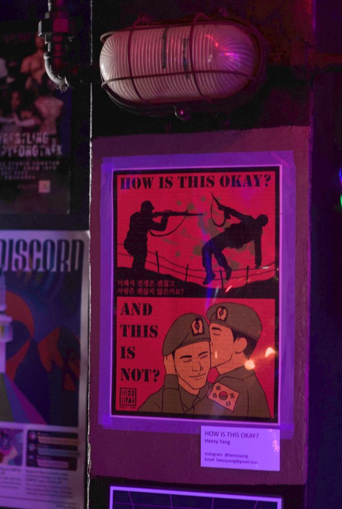 A sign that shows two silhouettes of soldiers shooting each other on top while on the bottom it’s two male soldiers kissing each other. The text says “why is this okay and this is not”