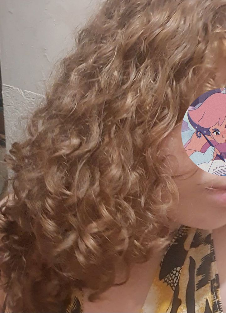 foto tirada há poucos minutos, com a qualidade mais baixa devido a iluminação artificial da lâmpada de teto. parte do meu rosto está coberta pela mesma figurinha, e o destaque continua sendo meu cabelo, agora já seco e com um pouquinho de frizz, porém ainda definido, formando cachos nas pontas e ondas na parte de cima 