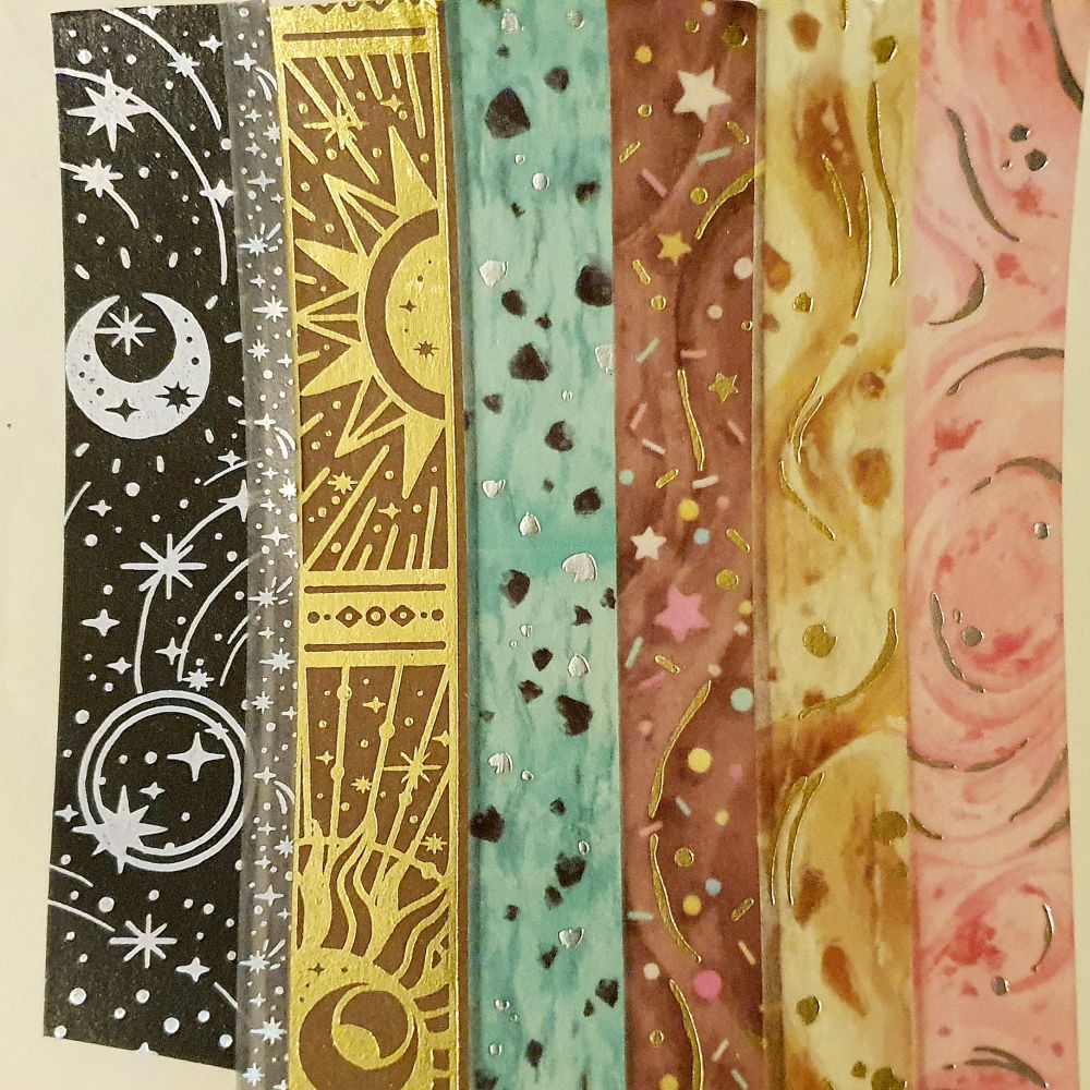 Photo of seven types of washi tape on paper, ranging from foil effect cosmic designs to ice cream (mint, choco, caramel, and strawberry)