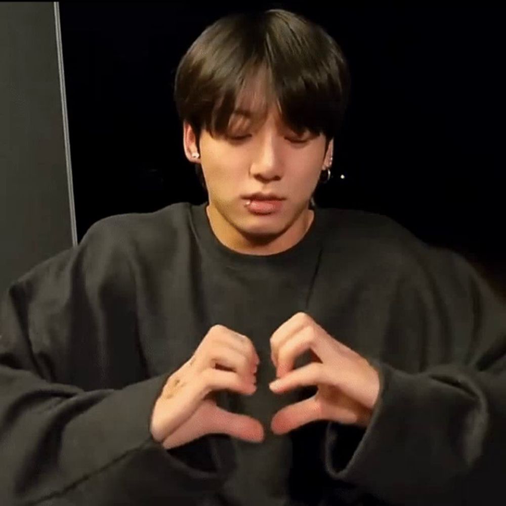 a young man is making a heart shape with his hands while wearing a black sweater .