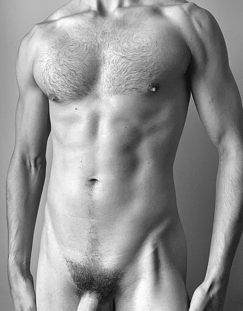 Black and white image of a naked man’s torso cropped from shoulders to thighs, showing hairy chest, bush, and a bit of shaft.