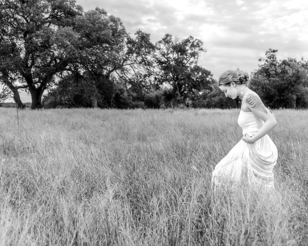 A young woman in a white dress walks through a field of tall grass. 