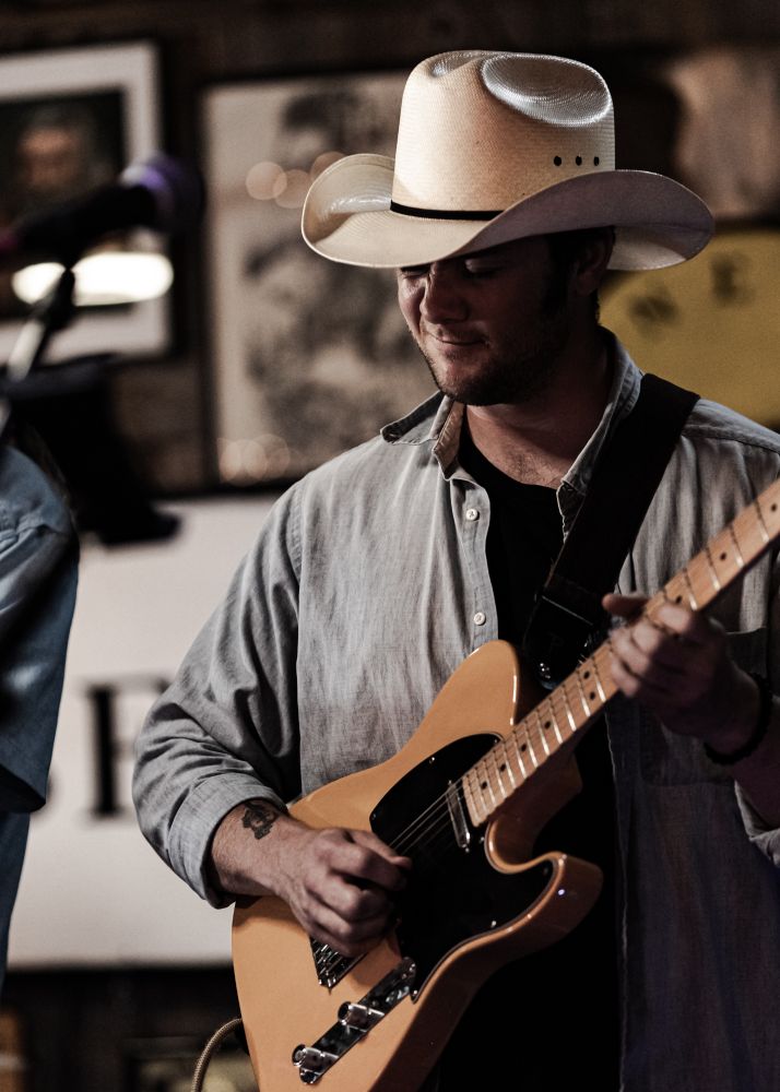 A guitarist makes a face while wearing a stetson and playing a Telecaster. 